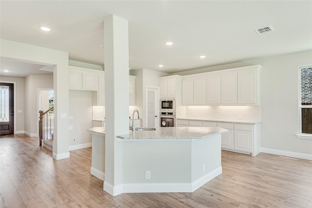 kitchen featuring oven, light wood-type flooring, white cabinets, black microwave, and sink