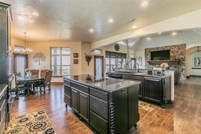 kitchen with a kitchen island, dark stone counters, decorative light fixtures, lofted ceiling, and dark hardwood / wood-style floors