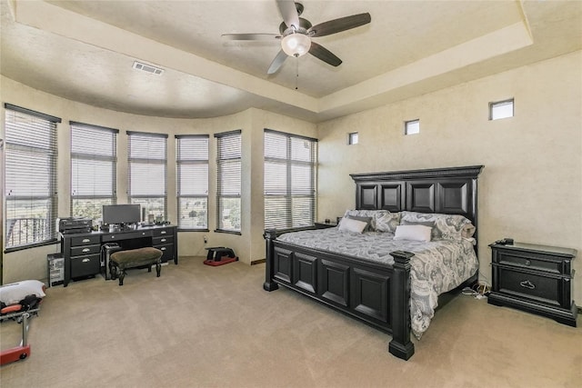 carpeted bedroom with ceiling fan and a raised ceiling