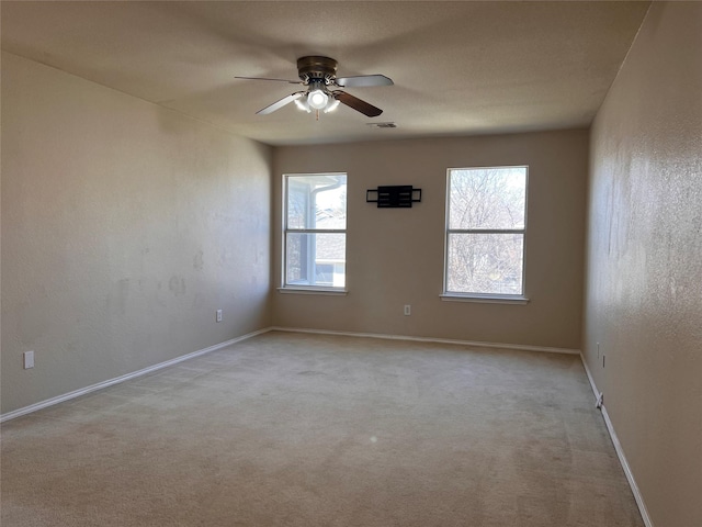 carpeted spare room featuring ceiling fan, plenty of natural light, visible vents, and baseboards