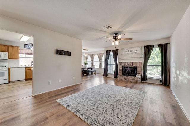 living room with light wood-style floors, a fireplace, visible vents, and a wealth of natural light