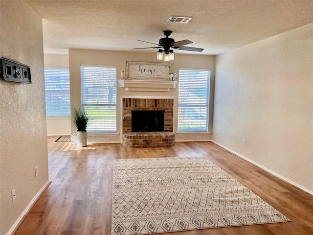 unfurnished living room featuring a textured ceiling, a brick fireplace, wood finished floors, and visible vents