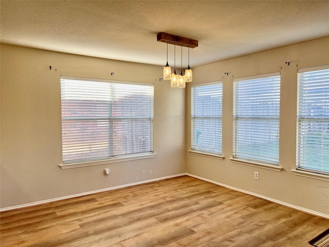 unfurnished room featuring a textured ceiling, baseboards, a chandelier, and wood finished floors