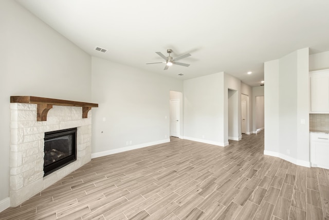 unfurnished living room featuring light hardwood / wood-style floors, ceiling fan, and a stone fireplace