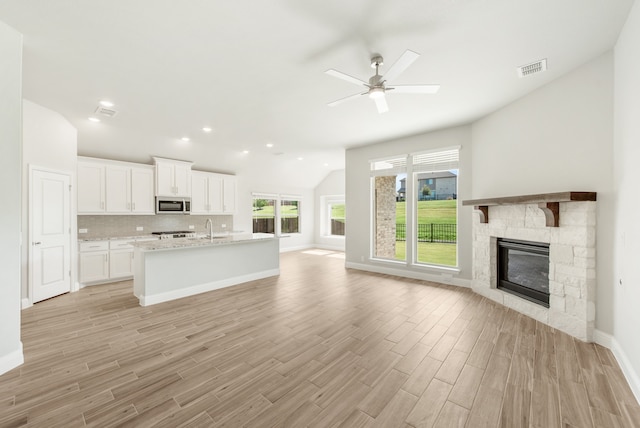 kitchen featuring vaulted ceiling, a stone fireplace, a kitchen island with sink, ceiling fan, and white cabinets