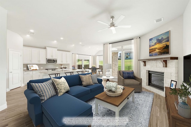 living room featuring light hardwood / wood-style floors, ceiling fan, and a stone fireplace