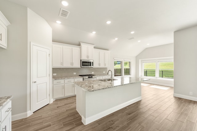 kitchen with an island with sink, stainless steel appliances, white cabinetry, and tasteful backsplash