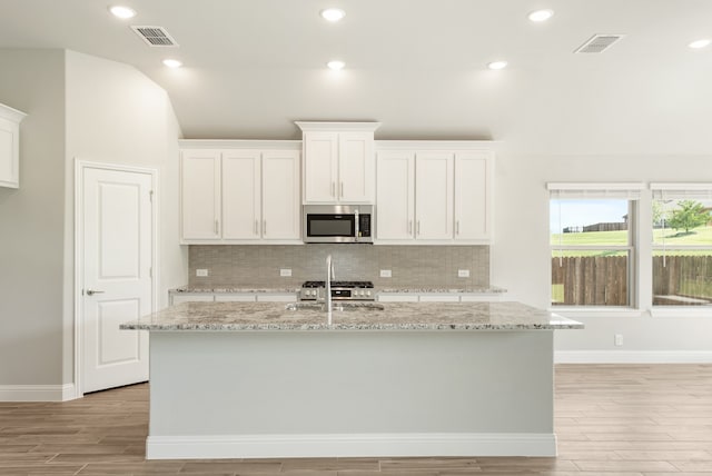 kitchen featuring white cabinetry, backsplash, light stone counters, an island with sink, and appliances with stainless steel finishes