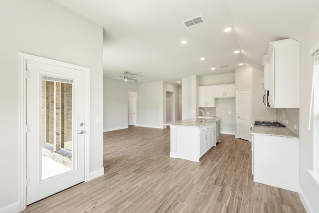 kitchen with vaulted ceiling, a center island with sink, decorative backsplash, ceiling fan, and white cabinets