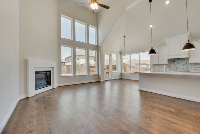 unfurnished living room with baseboards, a high ceiling, dark wood-style flooring, ceiling fan, and a glass covered fireplace