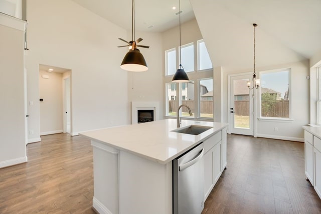 kitchen featuring a sink, dishwasher, a fireplace, wood finished floors, and a kitchen island with sink