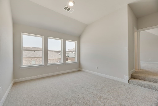 spare room featuring visible vents, baseboards, light colored carpet, and vaulted ceiling