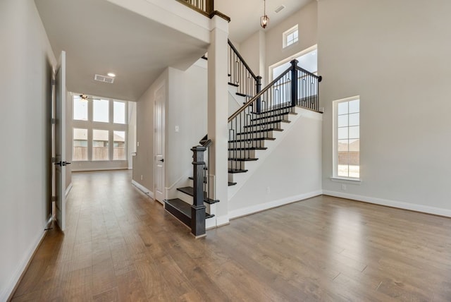 foyer with ceiling fan, a towering ceiling, and wood-type flooring