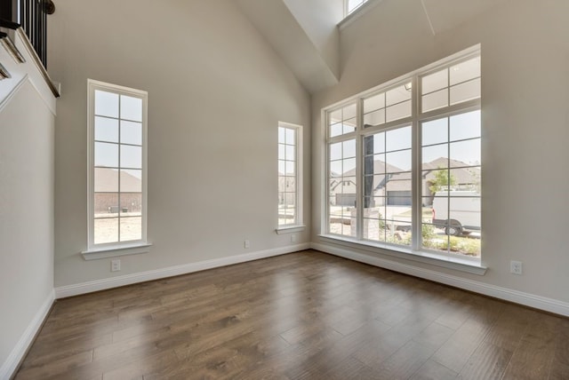 spare room with baseboards, dark wood-type flooring, and a towering ceiling