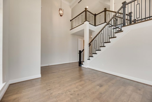 stairway featuring hardwood / wood-style floors, a towering ceiling, an inviting chandelier, and ornamental molding