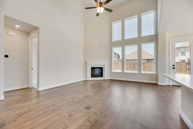 unfurnished living room featuring ceiling fan, a high ceiling, and light wood-type flooring