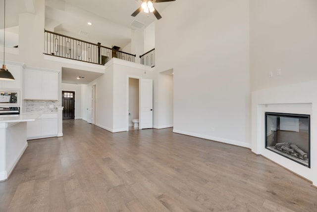 unfurnished living room with wood finished floors, baseboards, visible vents, a ceiling fan, and a glass covered fireplace