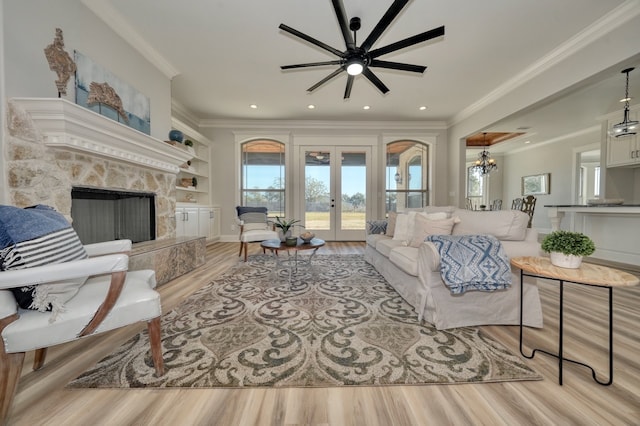 living room with french doors, a stone fireplace, ornamental molding, and light hardwood / wood-style flooring