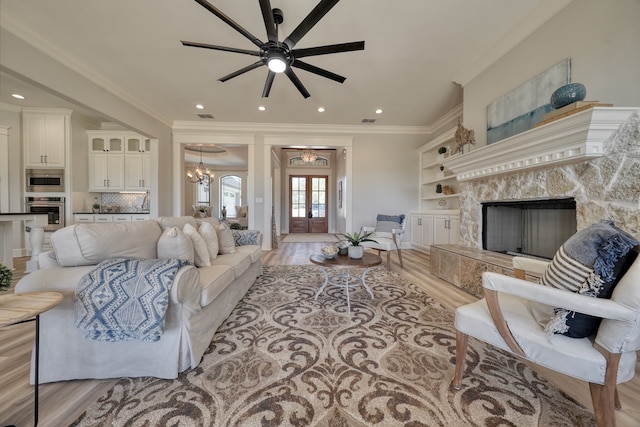 living room with a high end fireplace, light hardwood / wood-style flooring, ornamental molding, ceiling fan with notable chandelier, and french doors