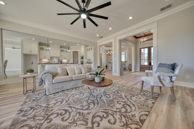 living room with crown molding, french doors, ceiling fan with notable chandelier, and light wood-type flooring