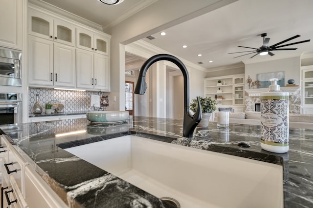 kitchen with white cabinetry, dark stone countertops, ornamental molding, and sink