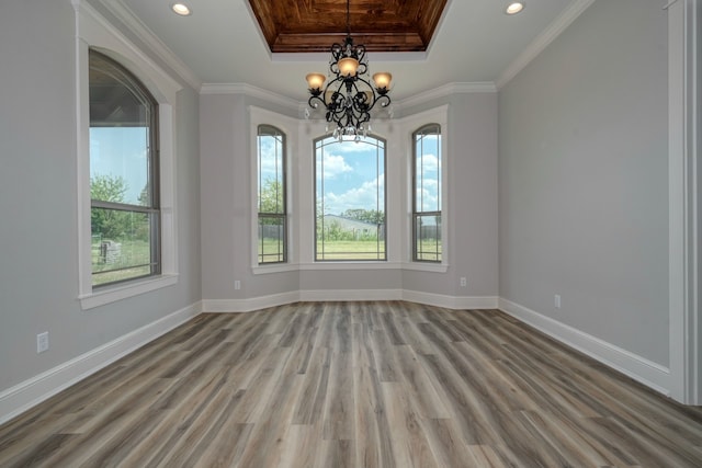 spare room with crown molding, hardwood / wood-style flooring, an inviting chandelier, and a raised ceiling