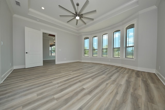 empty room featuring light hardwood / wood-style flooring, a tray ceiling, crown molding, and ceiling fan