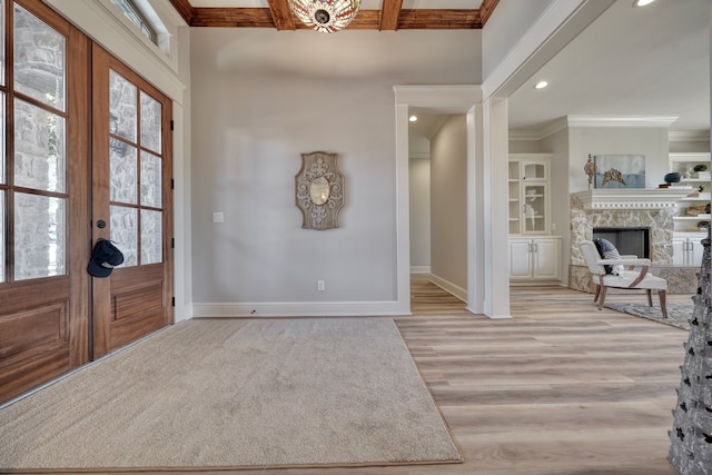 entrance foyer featuring beam ceiling, light wood-type flooring, ornamental molding, a fireplace, and french doors