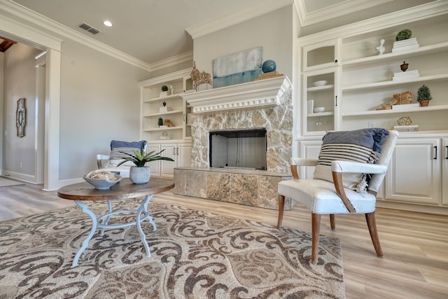 living room with built in features, light hardwood / wood-style flooring, a fireplace, and crown molding