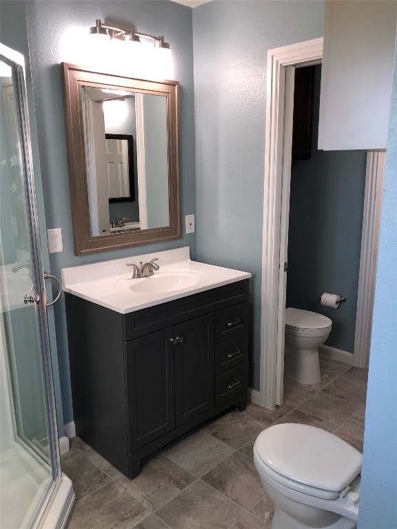 bathroom featuring a shower with door, vanity, toilet, and tile flooring