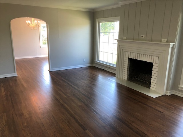 unfurnished living room featuring ornamental molding, dark hardwood / wood-style floors, a notable chandelier, and a fireplace