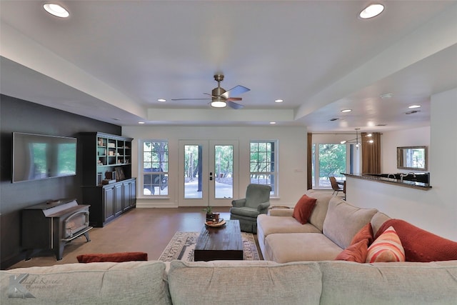 living room featuring a wood stove, wood-type flooring, french doors, a tray ceiling, and ceiling fan