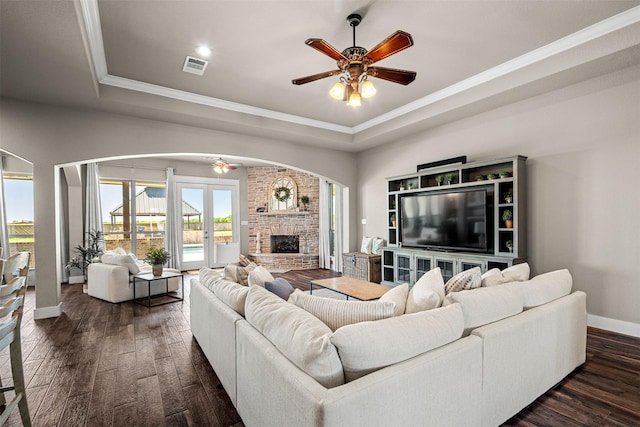 living room featuring ceiling fan, a fireplace, ornamental molding, dark hardwood / wood-style flooring, and a raised ceiling