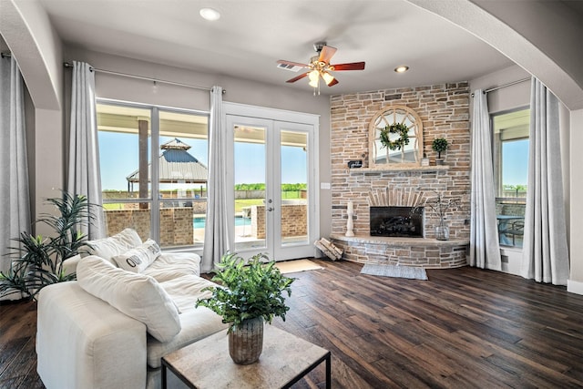 living room with a stone fireplace, dark hardwood / wood-style floors, ceiling fan, and french doors