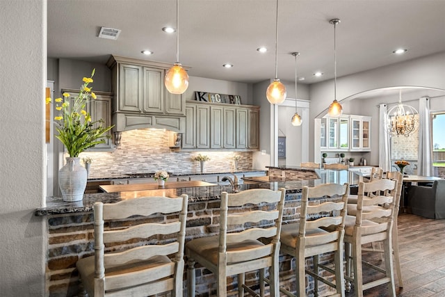 kitchen with pendant lighting, dark stone countertops, backsplash, a kitchen bar, and kitchen peninsula