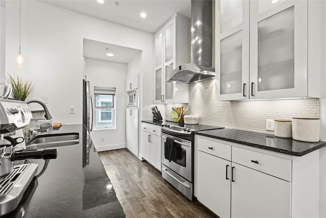 kitchen with wall chimney exhaust hood, hanging light fixtures, dark hardwood / wood-style floors, white cabinets, and appliances with stainless steel finishes