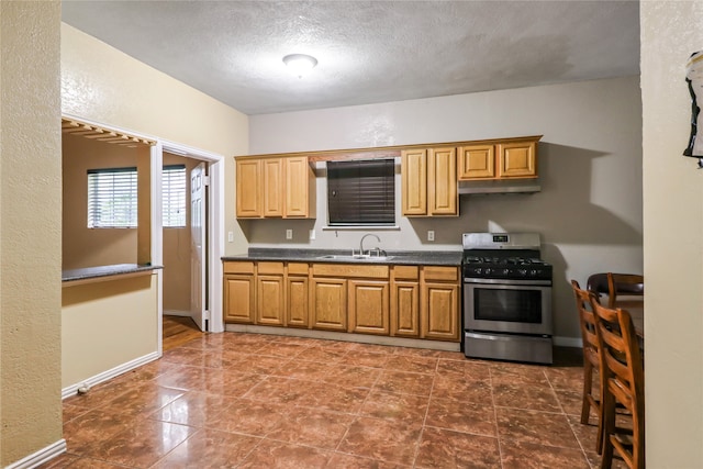 kitchen featuring sink, stainless steel gas range, dark tile floors, and a textured ceiling