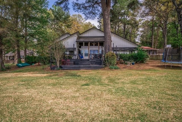 rear view of property featuring a trampoline and a yard