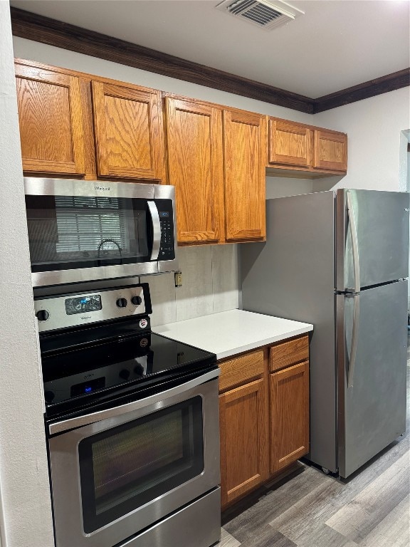 kitchen with crown molding, appliances with stainless steel finishes, and hardwood / wood-style floors