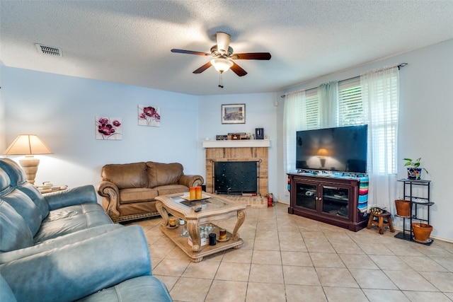 living room featuring a textured ceiling, a brick fireplace, ceiling fan, and light tile floors