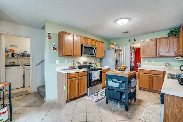 kitchen featuring appliances with stainless steel finishes, a textured ceiling, independent washer and dryer, sink, and light tile floors