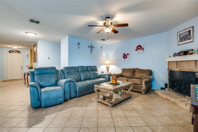 living room with ceiling fan, light tile flooring, a brick fireplace, and a textured ceiling