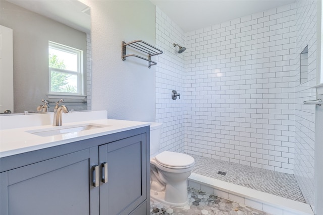 bathroom with tiled shower, toilet, tile floors, and vanity