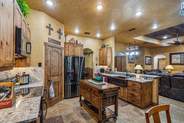 kitchen featuring light stone counters, pendant lighting, ceiling fan, sink, and stainless steel fridge with ice dispenser