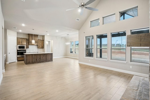 unfurnished living room with ceiling fan with notable chandelier, light hardwood / wood-style floors, high vaulted ceiling, and sink