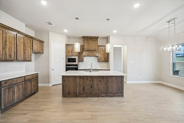 kitchen with stainless steel oven, a kitchen island with sink, built in microwave, and hanging light fixtures