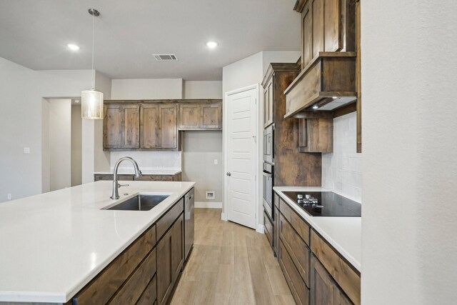 kitchen with tasteful backsplash, stainless steel appliances, sink, light hardwood / wood-style floors, and hanging light fixtures