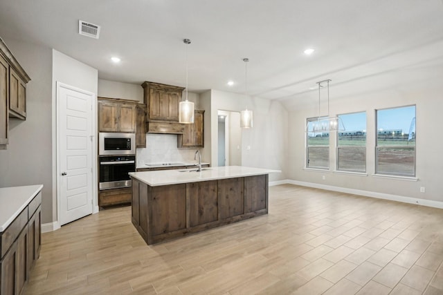 kitchen featuring built in microwave, sink, pendant lighting, a center island with sink, and oven