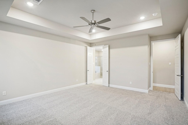 unfurnished bedroom featuring ceiling fan, light colored carpet, ensuite bath, and a tray ceiling