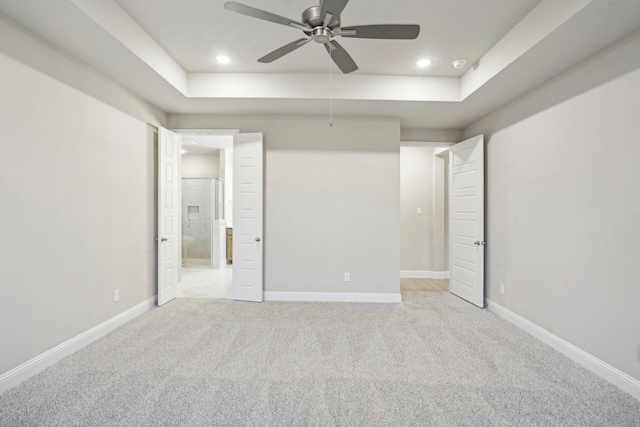 unfurnished bedroom featuring a raised ceiling, ensuite bath, ceiling fan, and light colored carpet